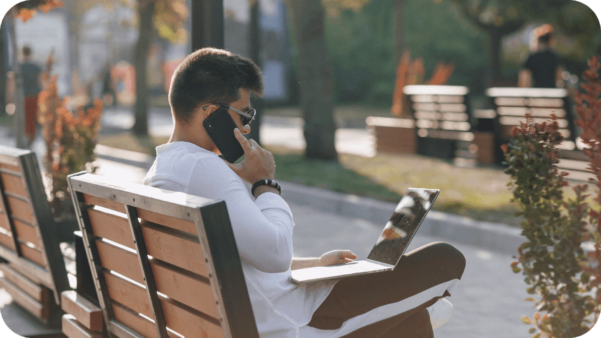 Young stylish guy in shirt with phone and notebook on bench on sunny day outdoors