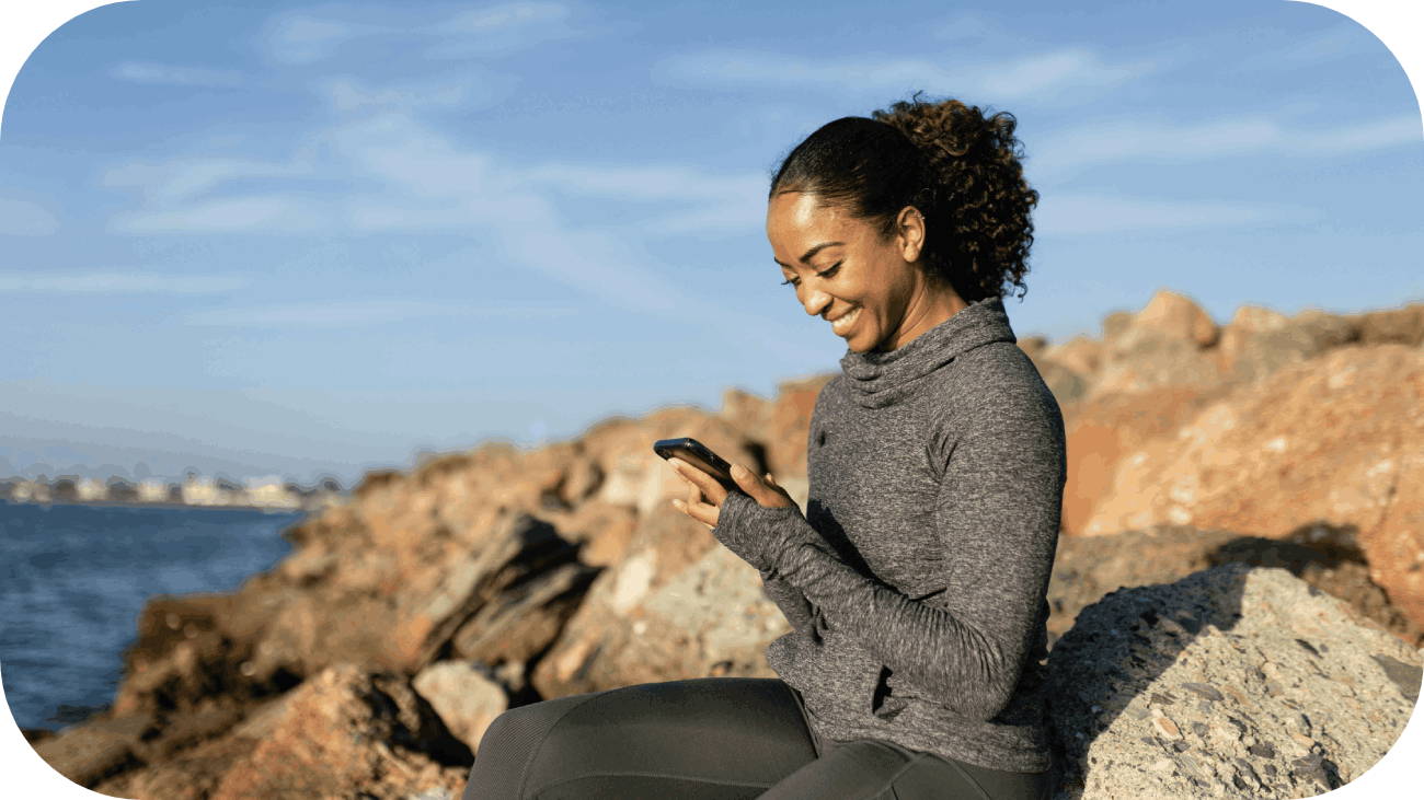 women sitting on a rock smiling and looking at her phone