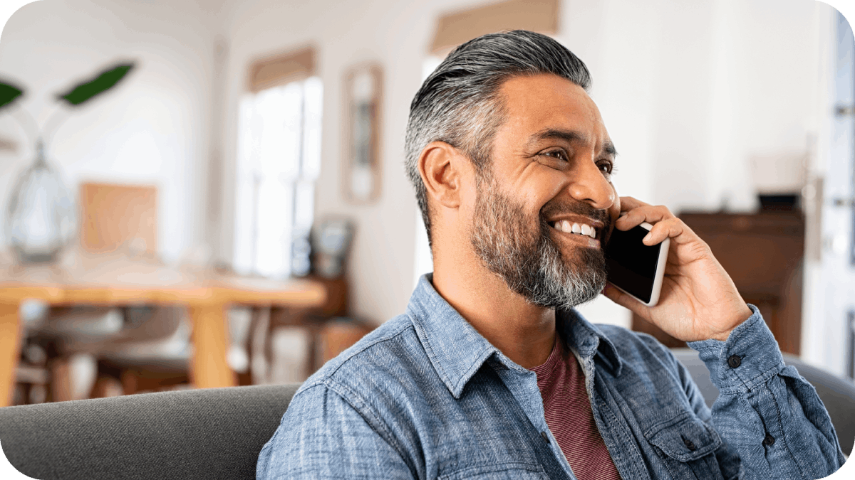 Indian man talking over smartphone while sitting on couch.