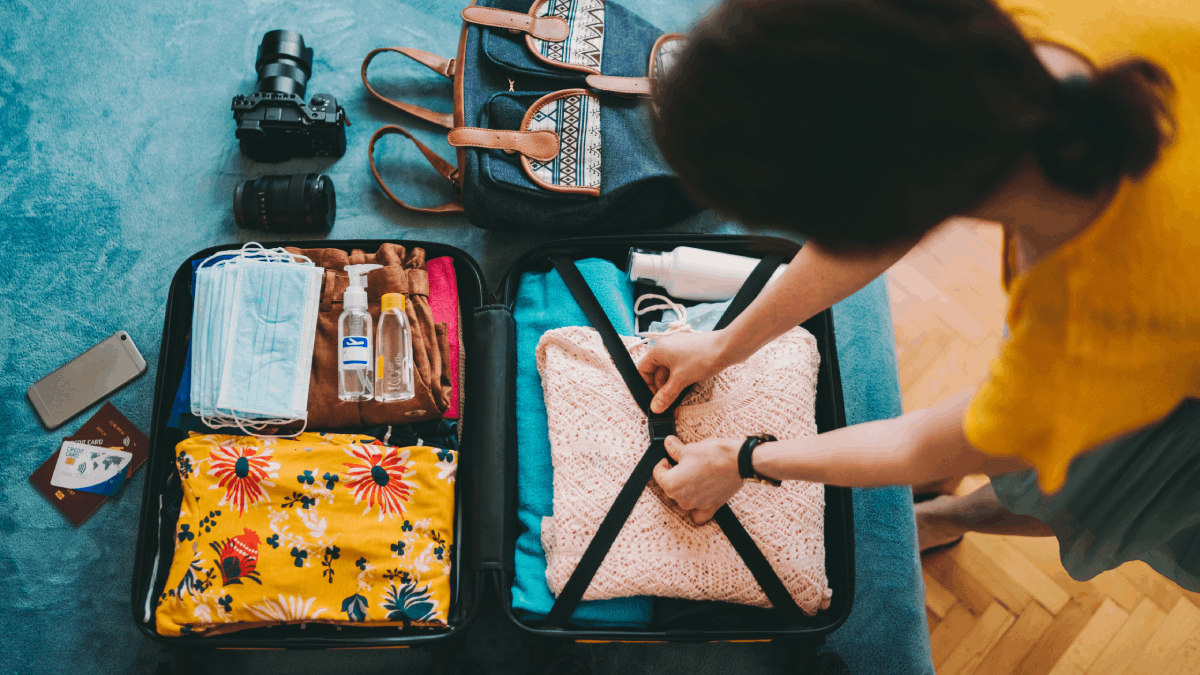 Woman packing suitcase for summer travel, including face masks and airplane travel-sized antibacterial hand gels.