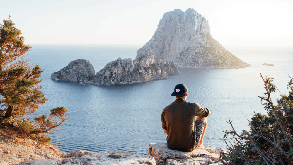 rear view of a man sitting on a cliff with a view of the sea