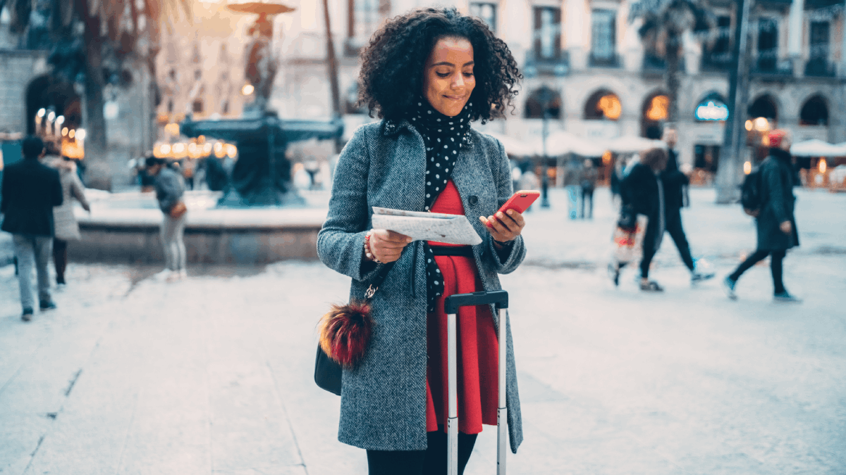 A stylish traveler with a suitcase checks her phone and map in a bustling city square, ready for her next adventure.