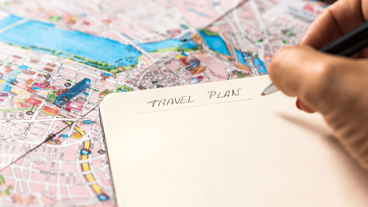 A close-up shot of a handwritten "Travel Plan" on a notebook, placed over a detailed city map, symbolizing organized travel planning.