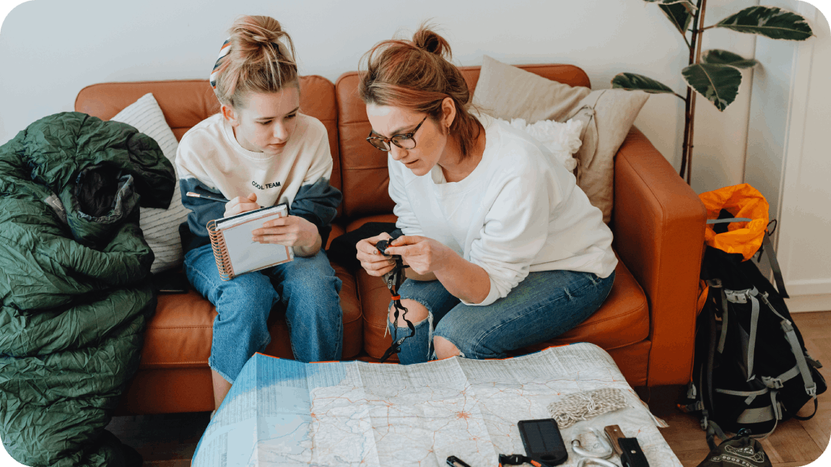 Mother and daughter preparing a travel plan together, surrounded by maps and gear, emphasizing teamwork and detailed planning.