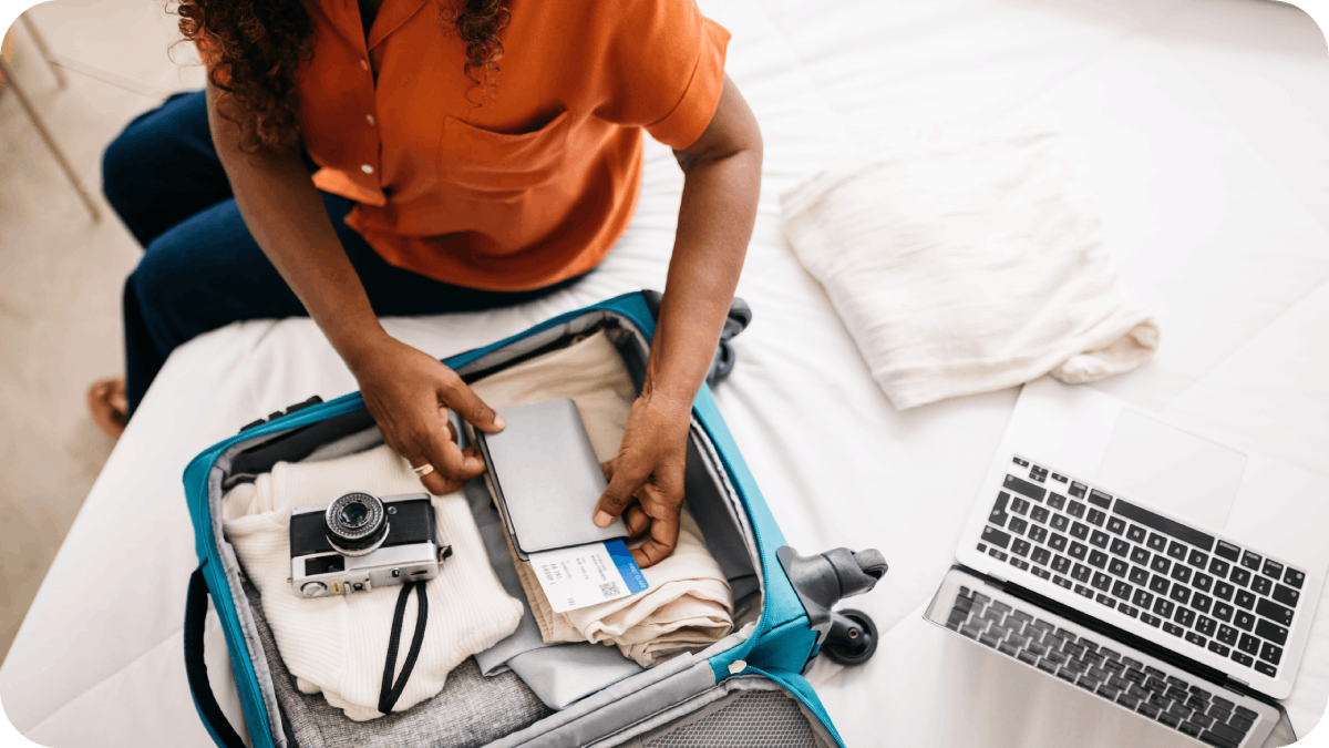 Traveler packing essentials into a suitcase alongside a camera and laptop for an organized journey.