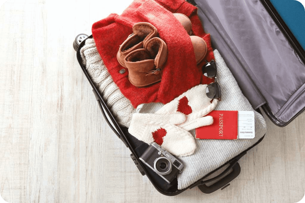 Open suitcase packed with winter essentials, including sweaters, boots, gloves, a scarf, and a passport, ready for a cozy winter getaway.