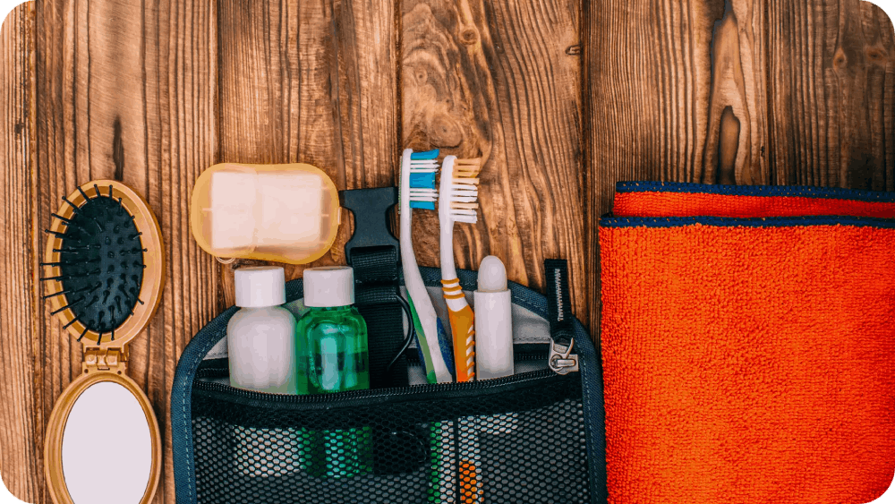 Travel toiletries kit with essentials like toothbrushes, soap, and bottles, placed on a wooden surface alongside a vibrant orange towel.