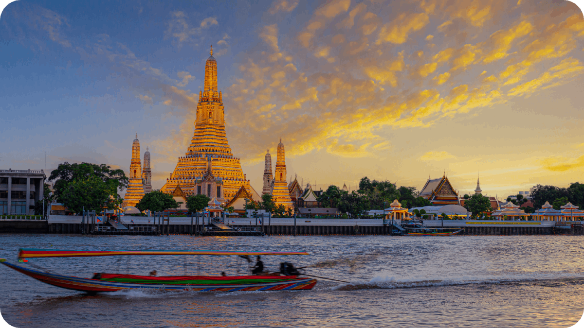 A vibrant sunset over Wat Arun temple in Bangkok, with a long-tail boat speeding along the Chao Phraya River.