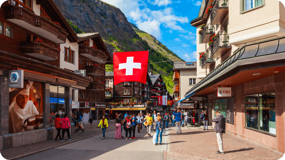 A lively street scene in Zermatt, Switzerland, with Swiss flags, traditional chalets, and a mountain backdrop.