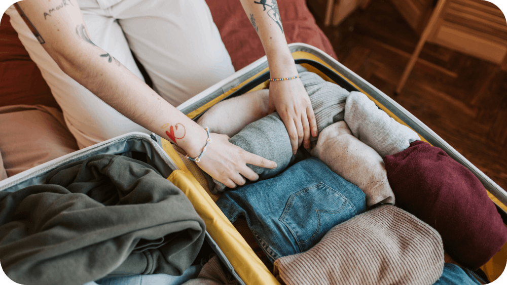 Person folding clothes and packing his luggage while packing for Winter travel